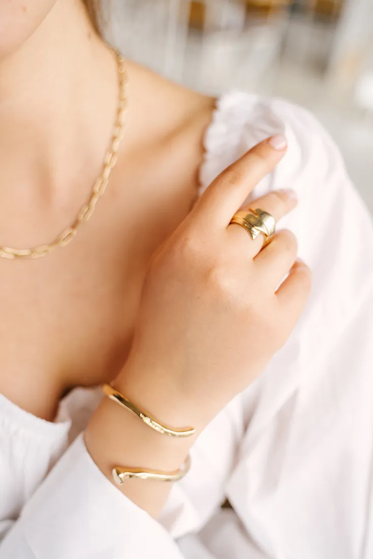 Close-up of a woman's hand showcasing gold jewelry: a necklace, ring, and bracelet.