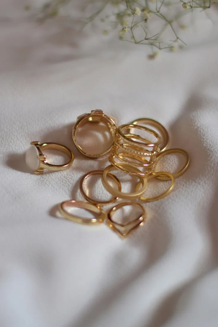 A collection of gold rings displayed on a soft surface, featuring various styles and a prominent stone ring.