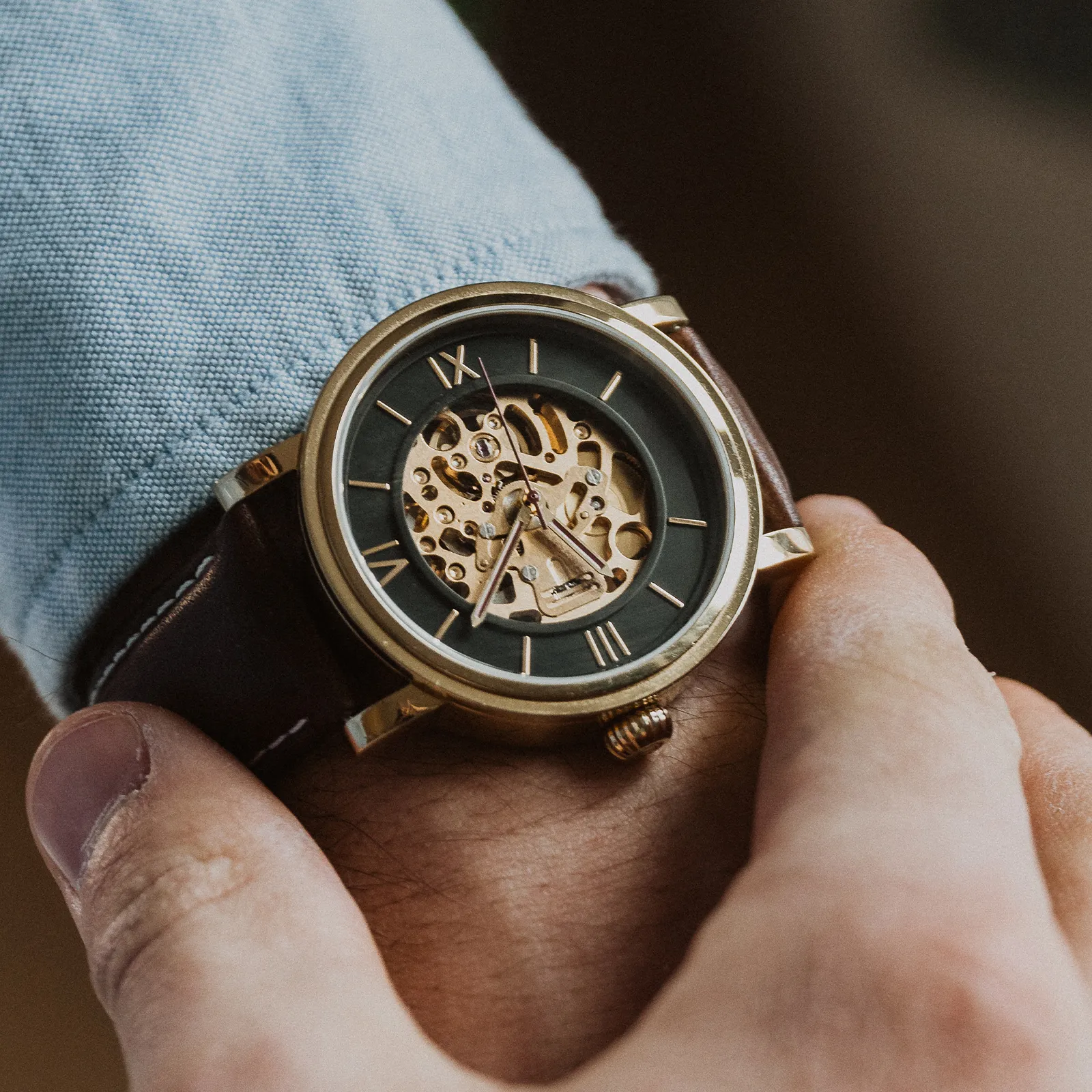 A gold skeleton watch with a brown leather strap on a person's wrist.