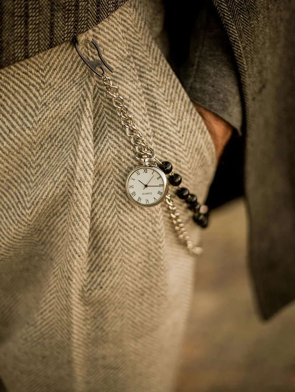 Close-up of a pocket watch with a chain on a herringbone fabric.