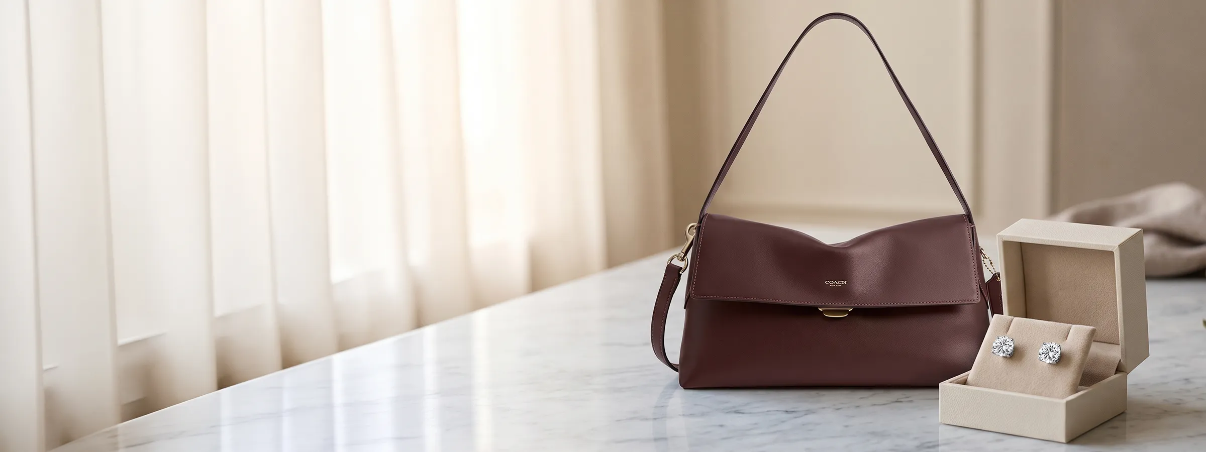 A brown handbag and a pair of earrings in a box on a marble surface.