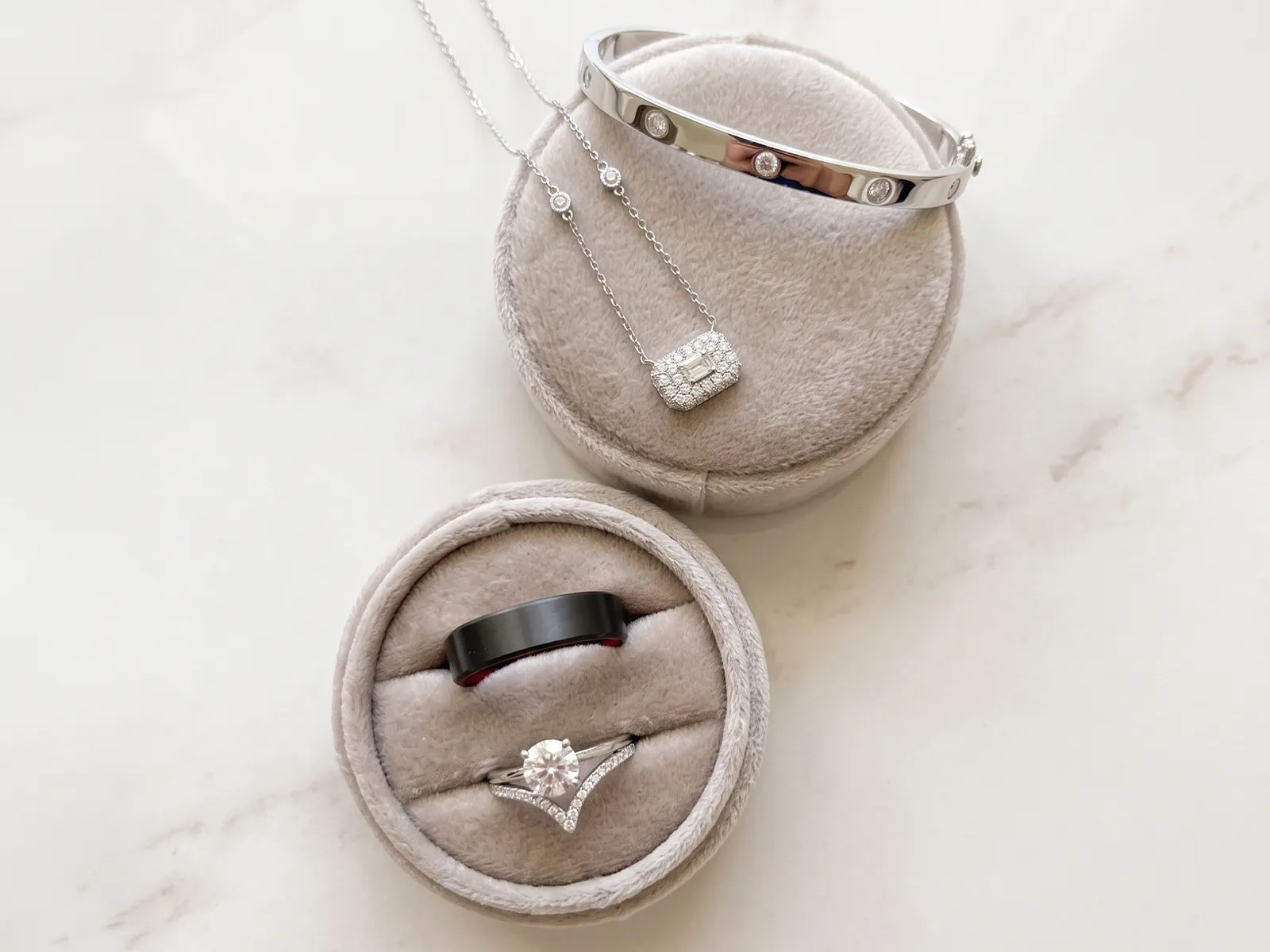 Two round jewelry boxes with a bracelet, necklace, and rings displayed on a light surface.