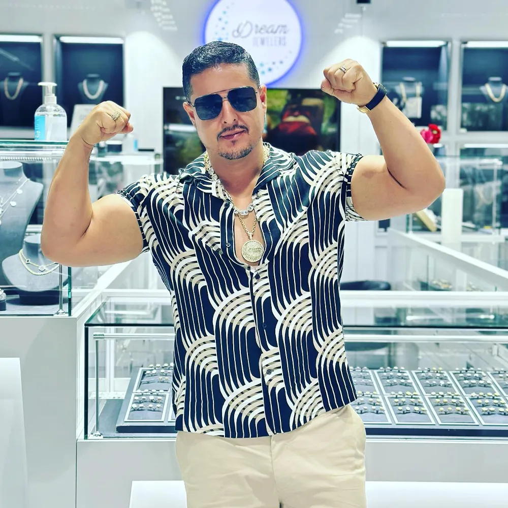 Man flexing muscles in a stylish shirt at Dream Jewelers, showcasing jewelry in the background.