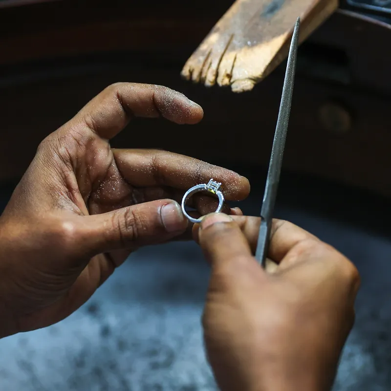 Jeweler shaping a silver engagement ring with a file, showcasing craftsmanship.