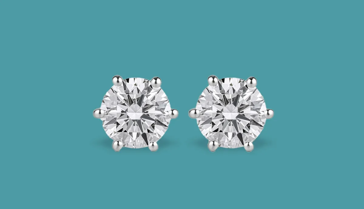 Round diamond stud earrings set in white gold against a teal background.