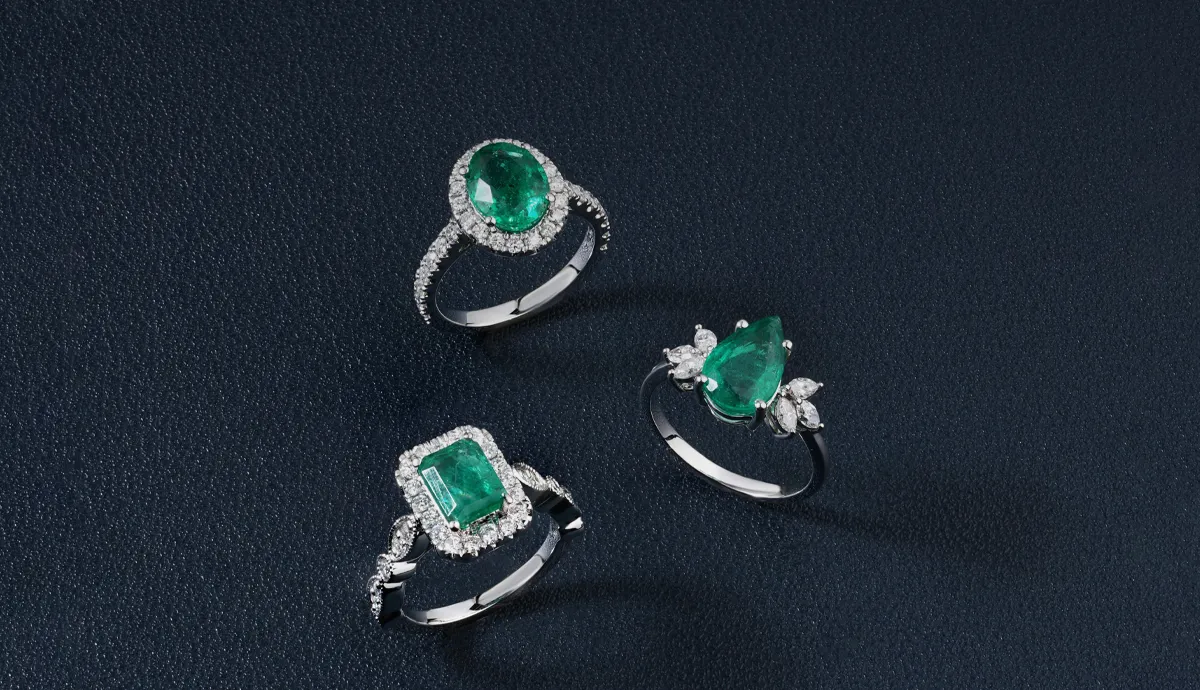Three elegant rings featuring emeralds and diamonds on a dark background, showcasing fine jewelry.