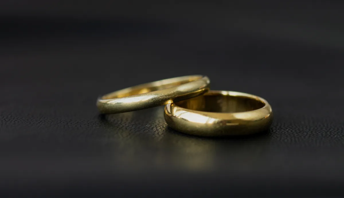 Two gold wedding bands resting on a dark surface, symbolizing love and commitment.