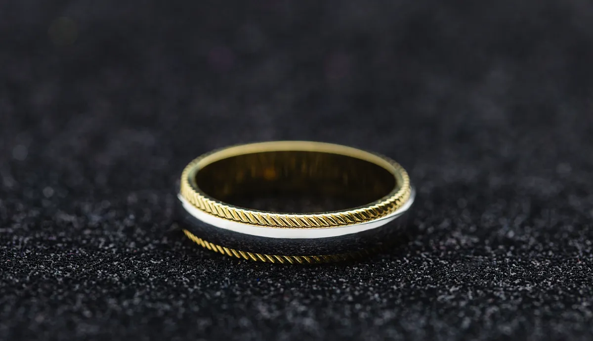 Elegant gold and silver wedding band displayed on a dark background.