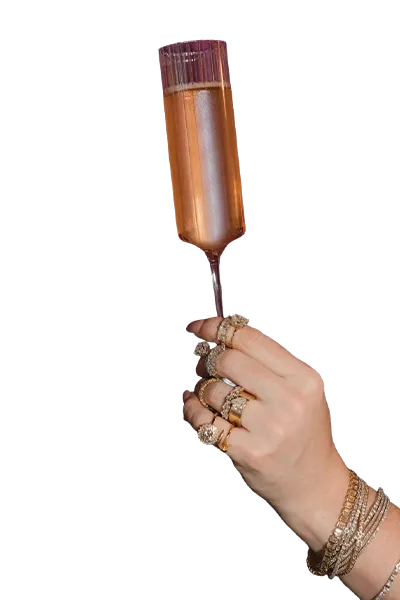 Woman holding champagne flute wearing bracelets and rings. 