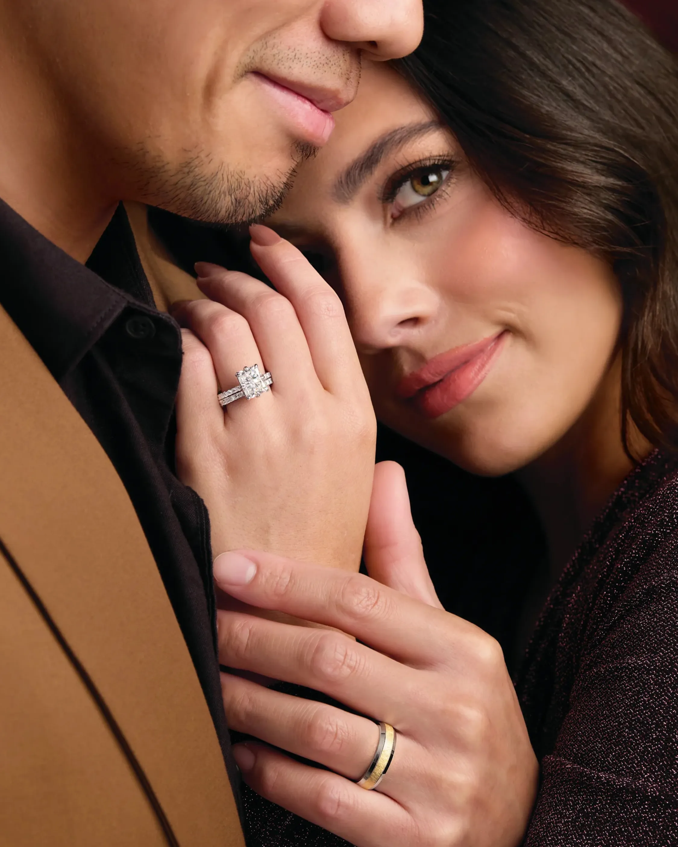 A couple holding hands, showcasing an engagement ring, surrounded by festive decorations. Visit Duke's Jewelers for fine jewelry