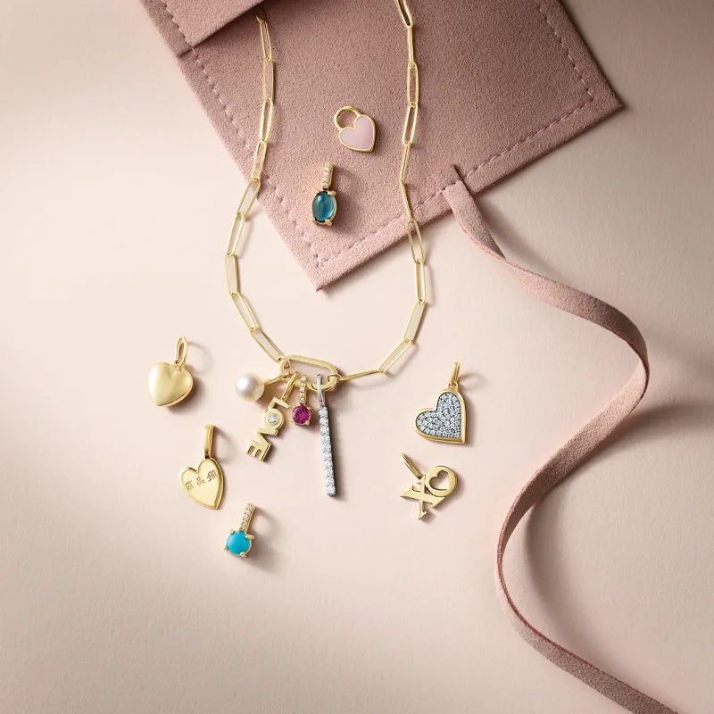 Gold charm necklace with various colorful pendants on a soft pink background.