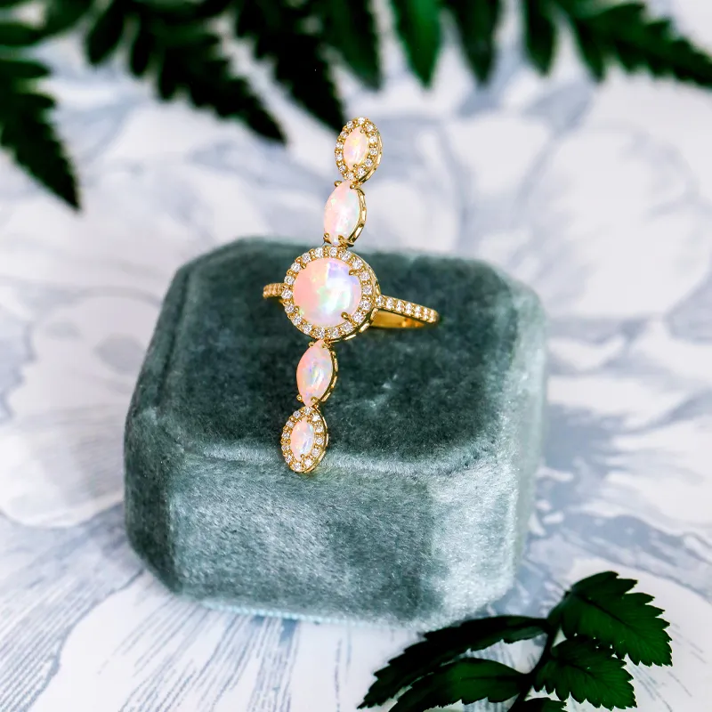 Gold ring with opal stones and diamonds, displayed on a gray velvet box.