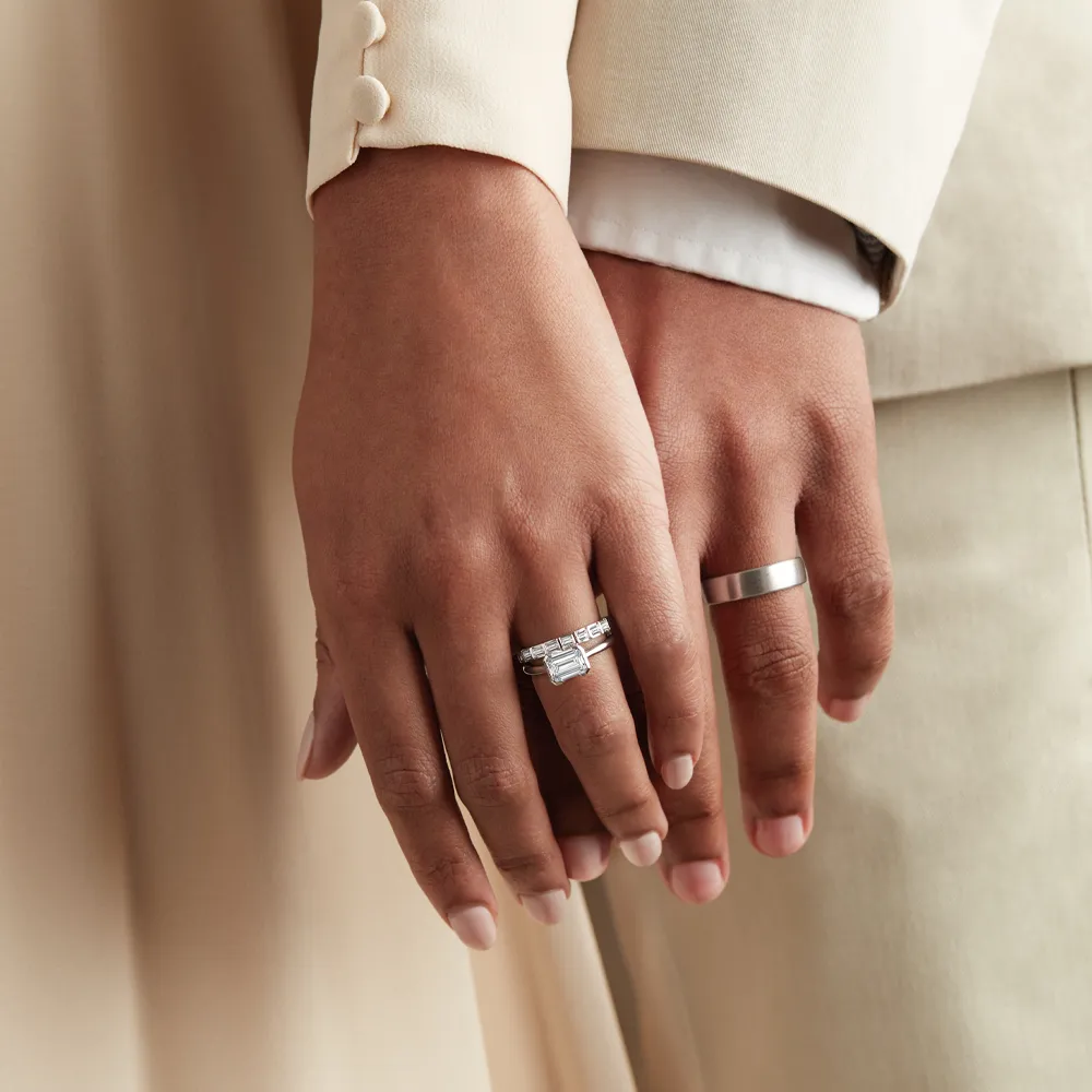 A close-up of two hands holding, one with a diamond engagement ring and the other with a simple wedding band.
