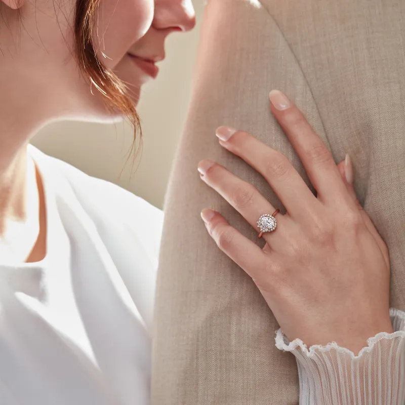 A woman shows off her engagement ring while leaning against a man's shoulder, symbolizing love and commitment.