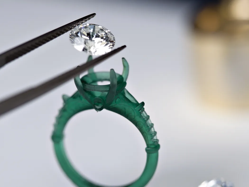 A jeweler using tweezers to place a diamond on a green ring setting.