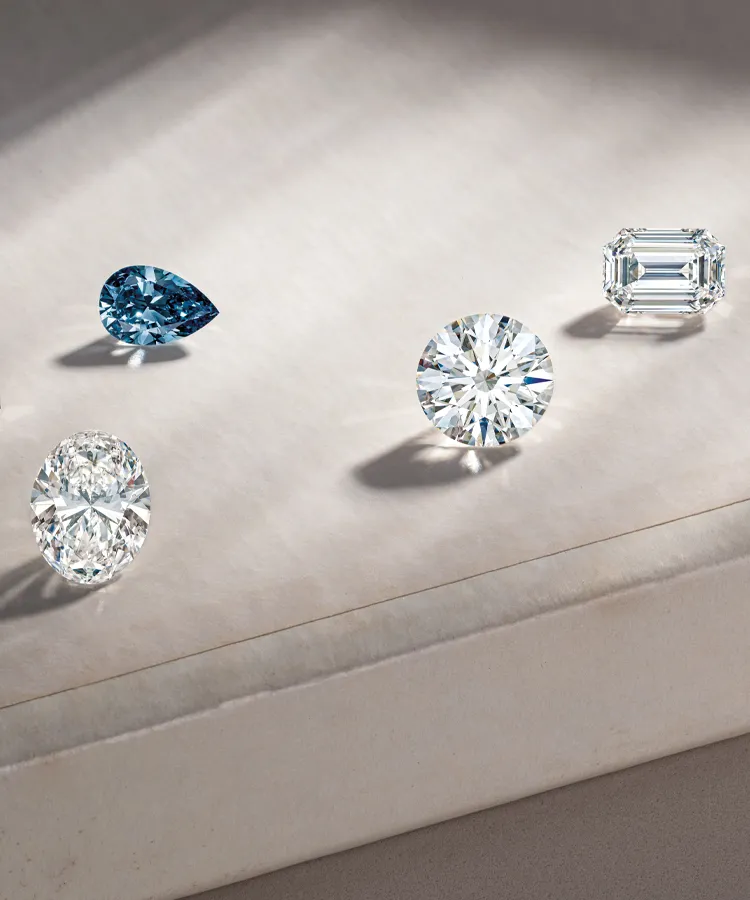 Four stunning diamonds in various cuts displayed on a soft surface, showcasing their brilliance and clarity.