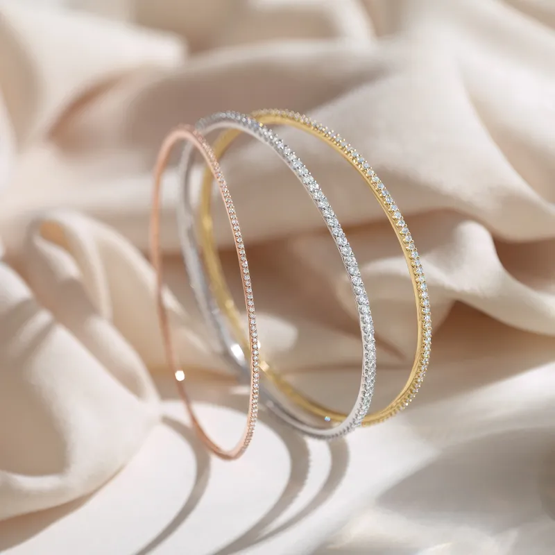 Three elegant bracelets in rose gold, silver, and gold with sparkling accents, displayed on soft fabric.