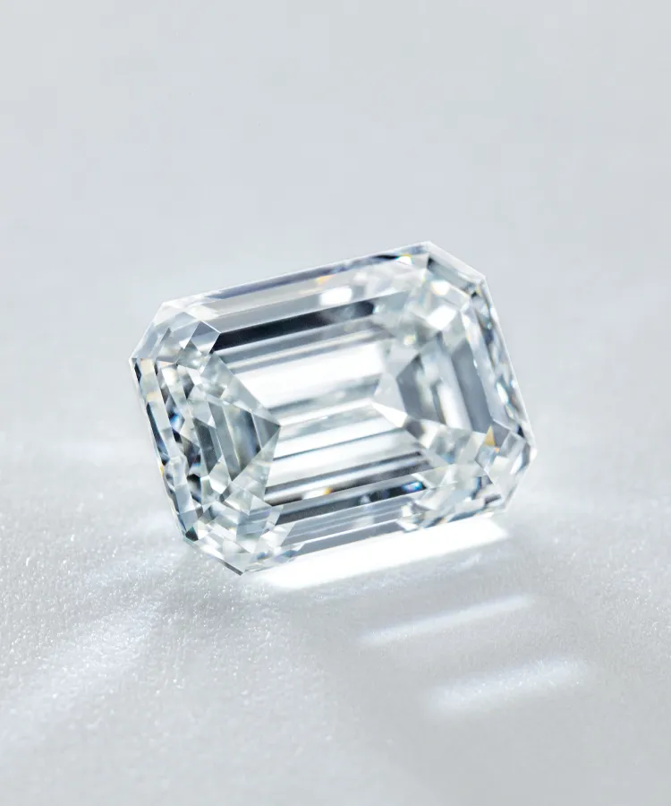 Clear emerald-cut diamond resting on a light surface, showcasing its brilliance and clarity.