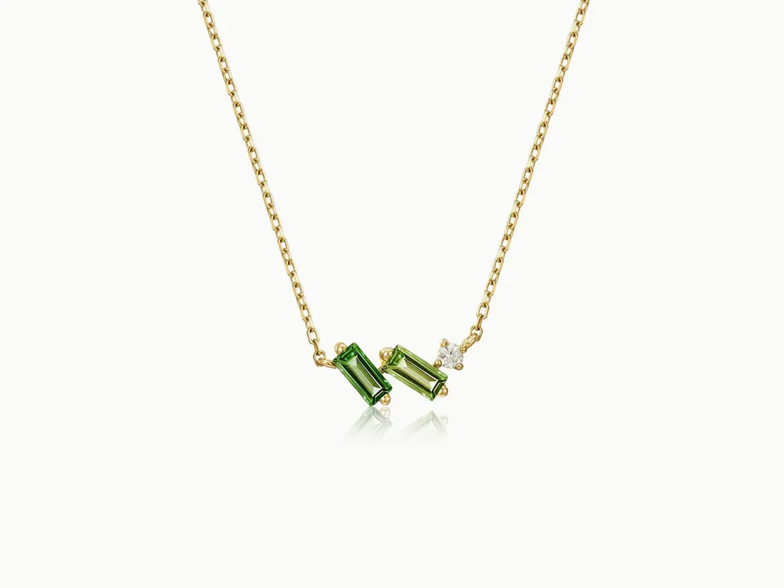 Elegant gold necklace featuring two green gemstones and a diamond accent. Click to explore more necklaces.