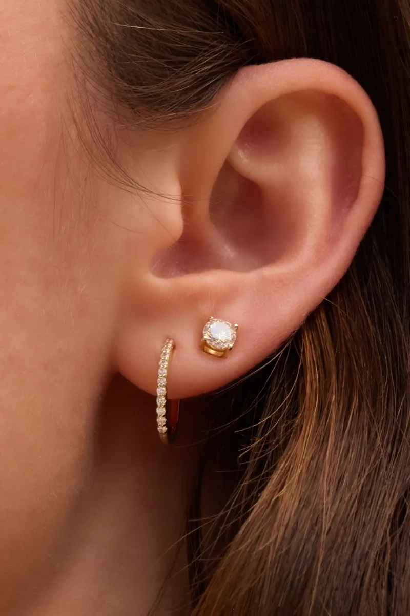 Close-up of a woman's ear featuring a gold hoop earring and a sparkling stud earring. Shop at E.G. Landis Jewelers, Gilbertsvill