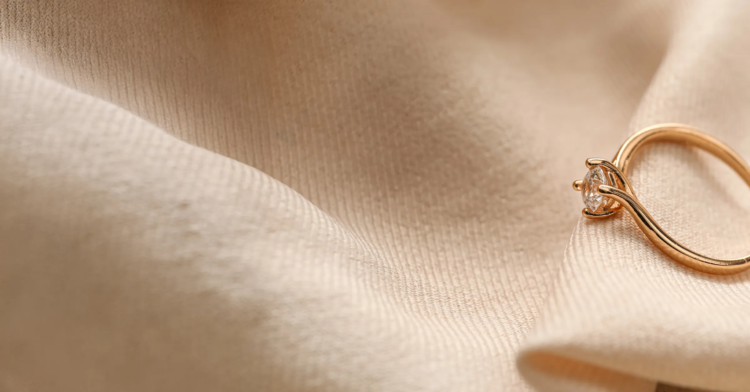 Close-up of a gold engagement ring with a diamond on soft beige fabric.