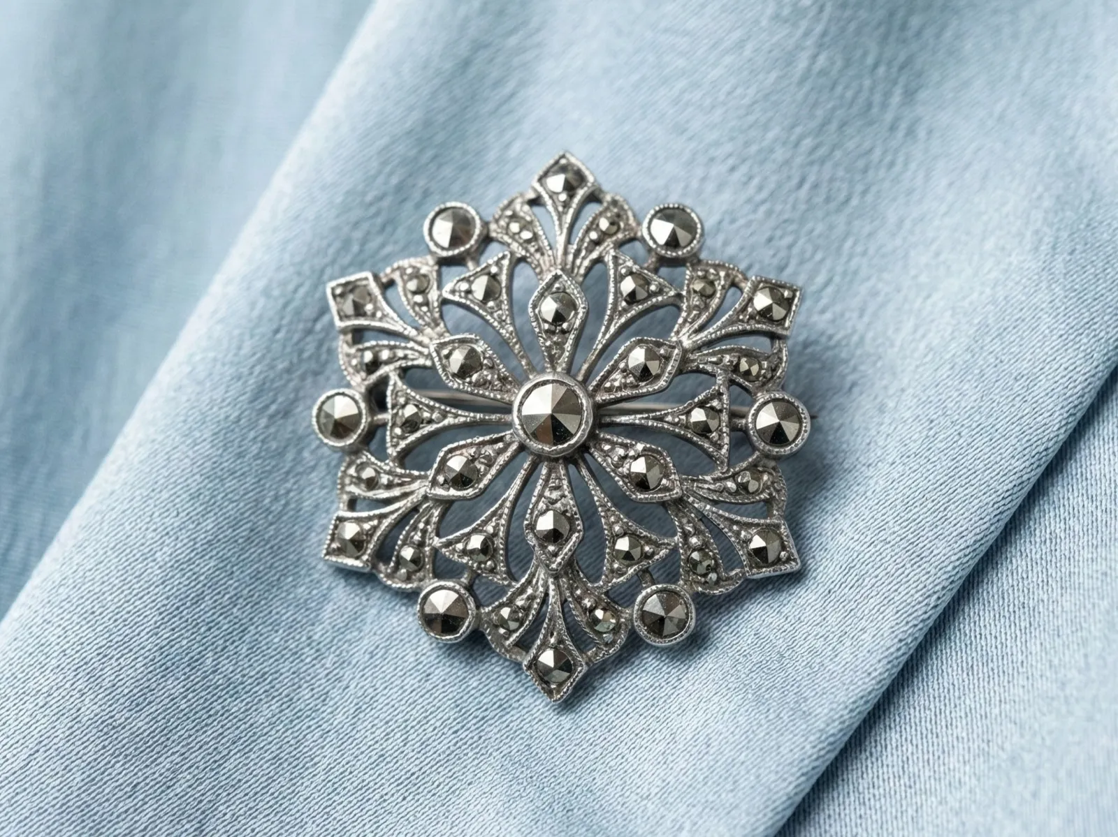 Intricate silver brooch with sparkling details on a light blue fabric background at E.G. Landis Jewelers, Gilbertsville.