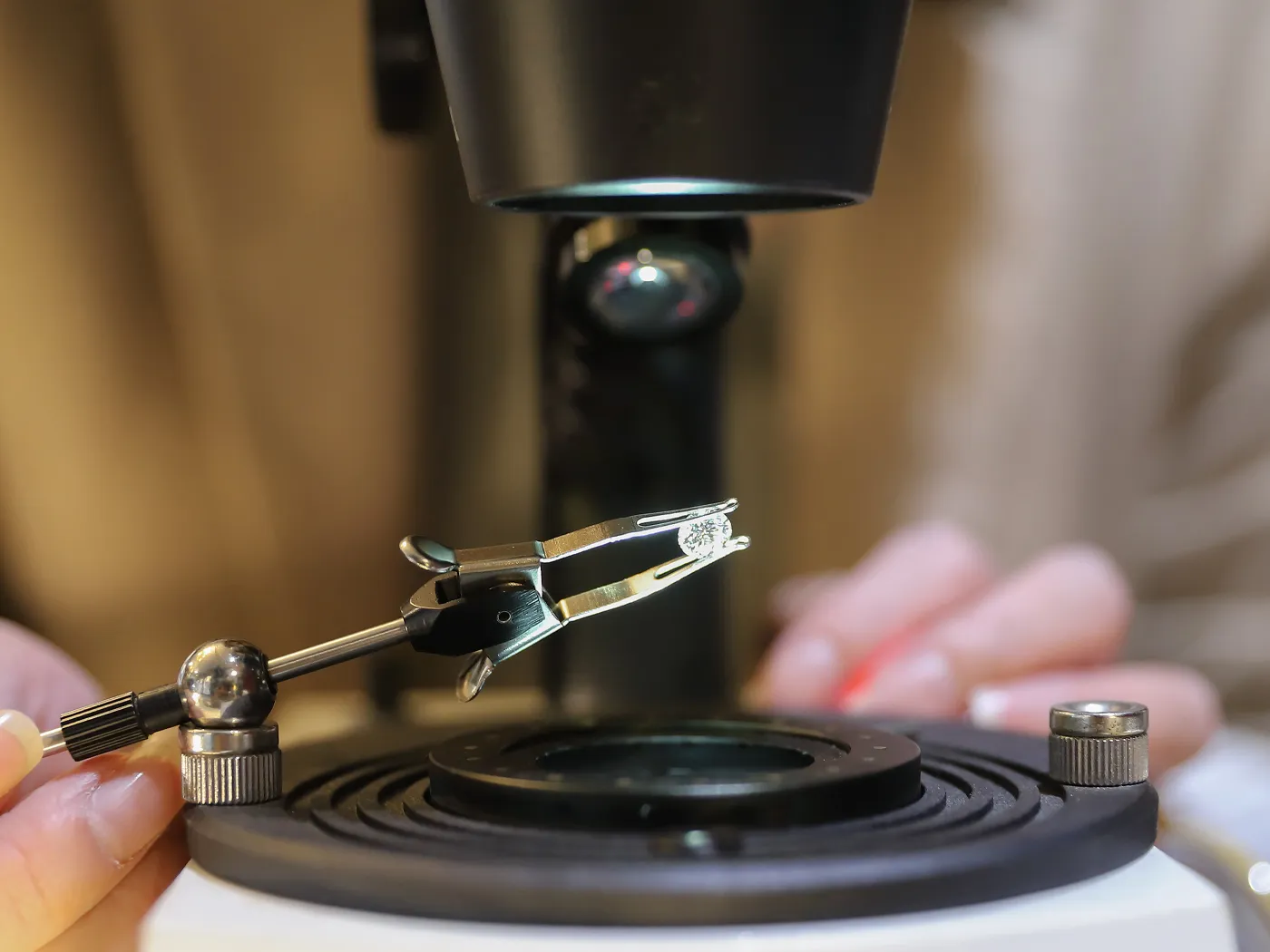 Jewelry appraisal process with a microscope and tweezers, showcasing a diamond. Learn more about our appraisal services.