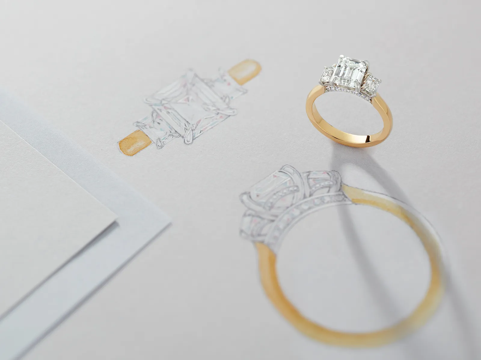 A diamond engagement ring next to its sketch on paper.