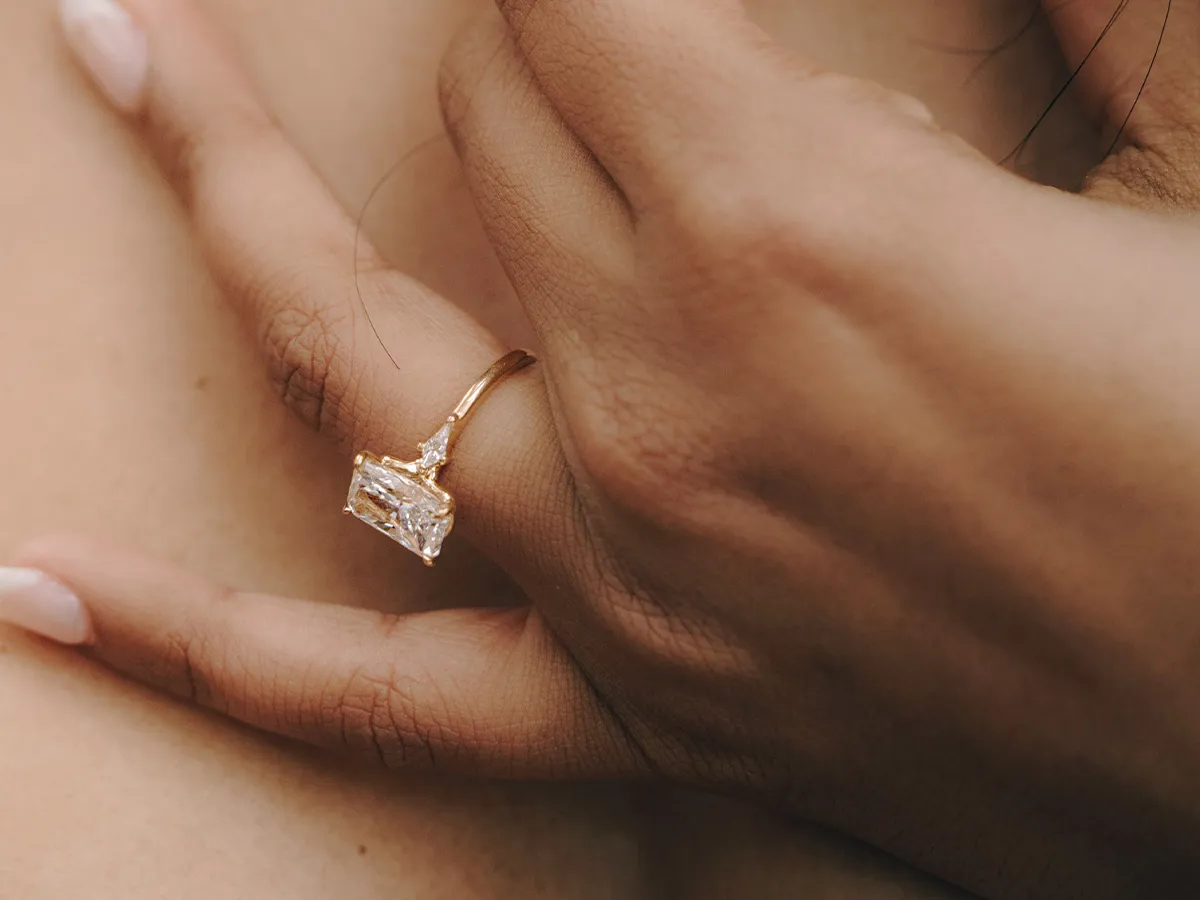 A hand wearing a gold ring with a large rectangular diamond.