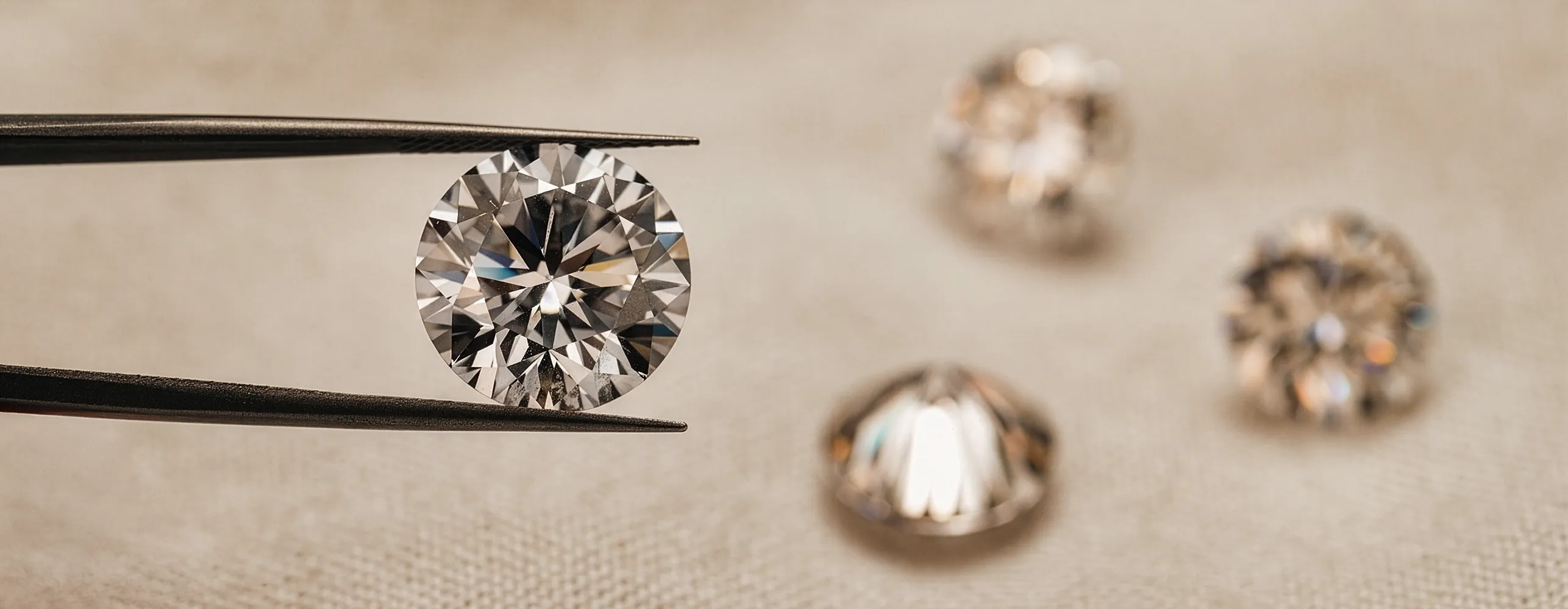 Diamond held by tweezers with three more diamonds blurred in the background. Browse the Inventory.
