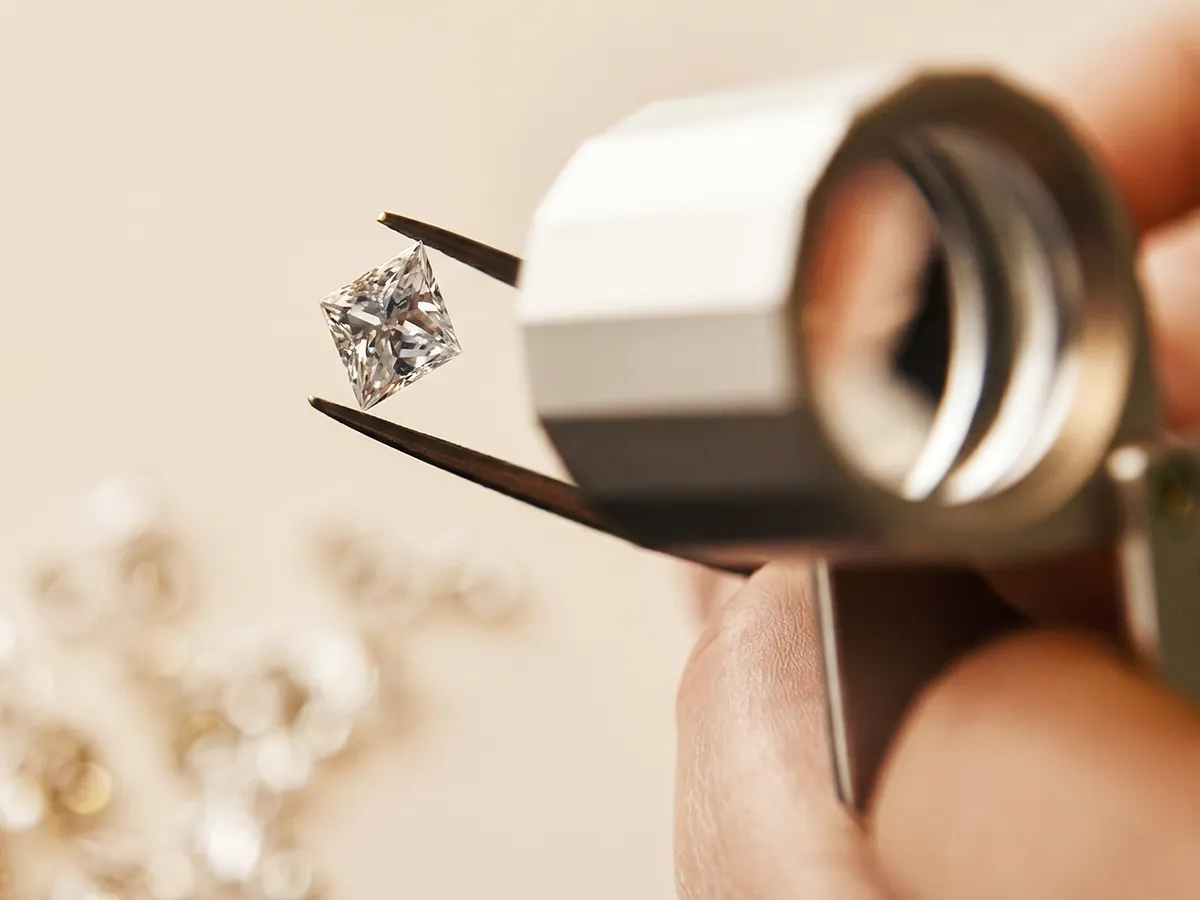 Diamond held by tweezers under magnifying glass. Learn more.