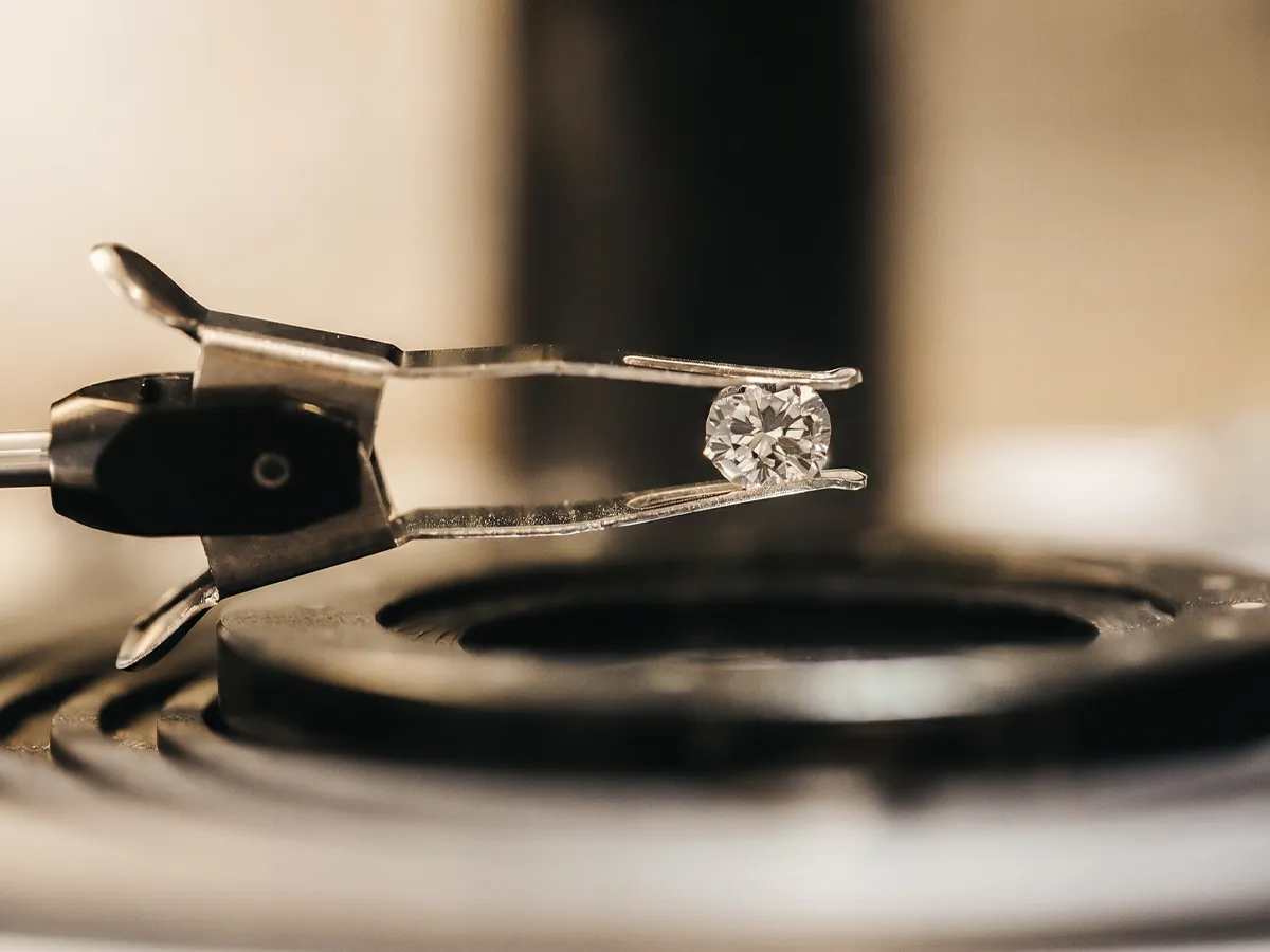 Diamond held by tweezers over a machine. Click to learn more about lab-grown vs. natural diamonds.