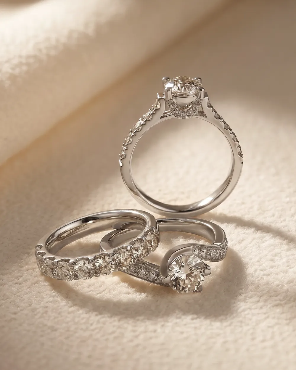 Three diamond engagement rings on a soft fabric background. Click to 