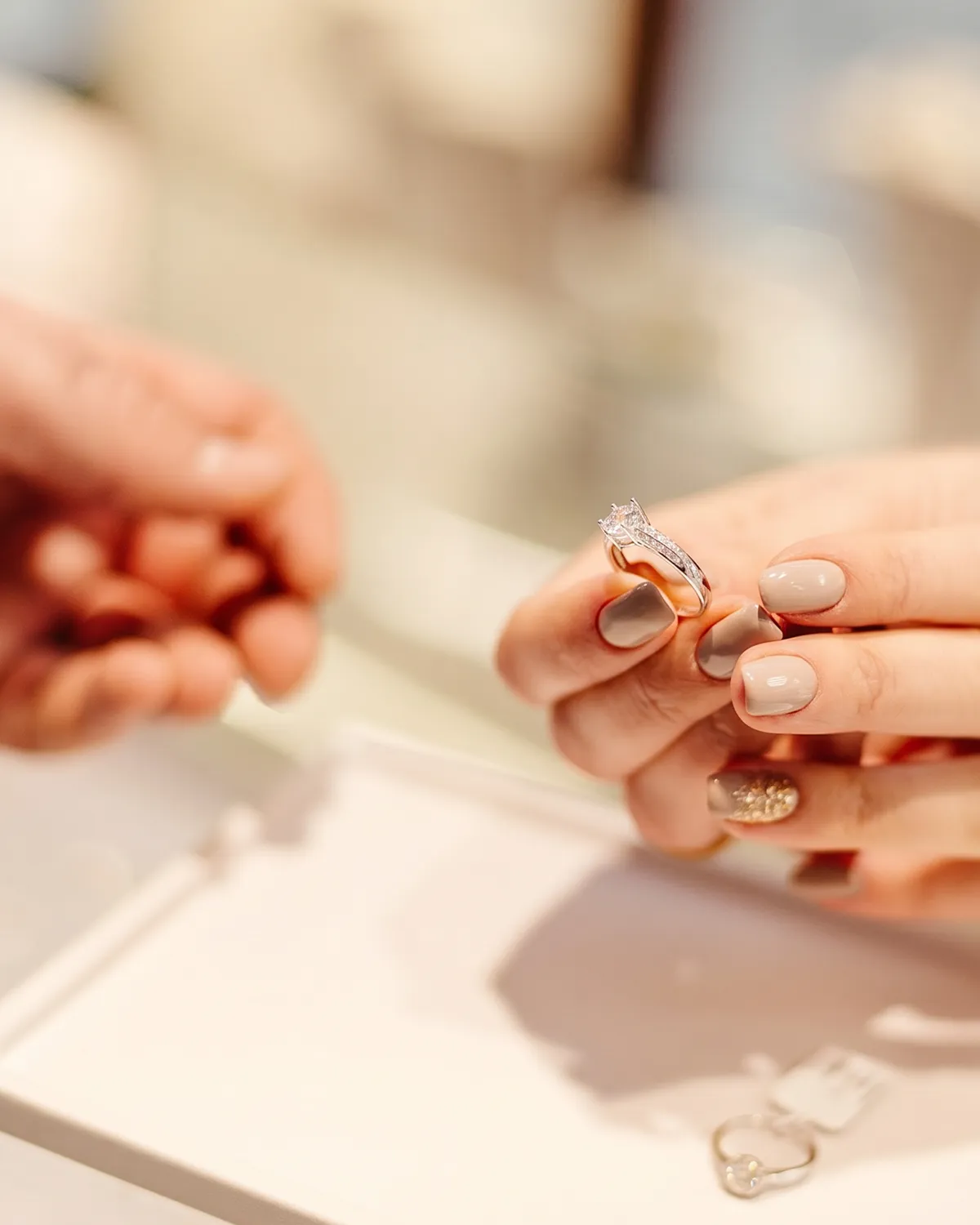 Hands holding a diamond ring in a jewelry store setting.