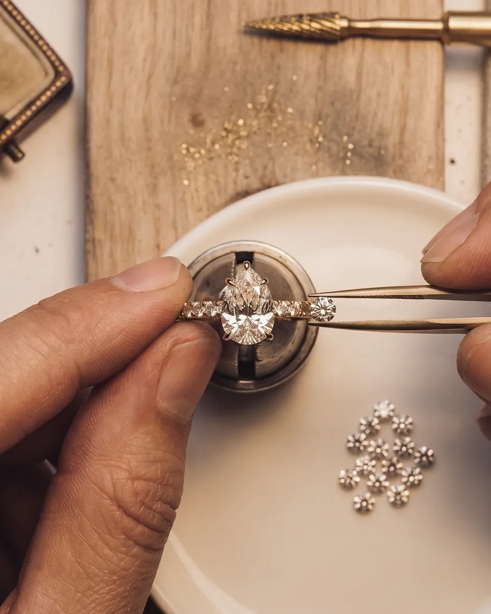 Hands crafting a diamond ring on a wooden table.