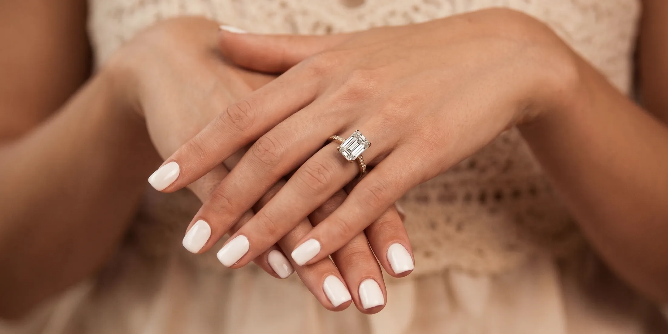 Hands with white nails displaying an emerald-cut diamond ring. Book a Virtual Consultation.