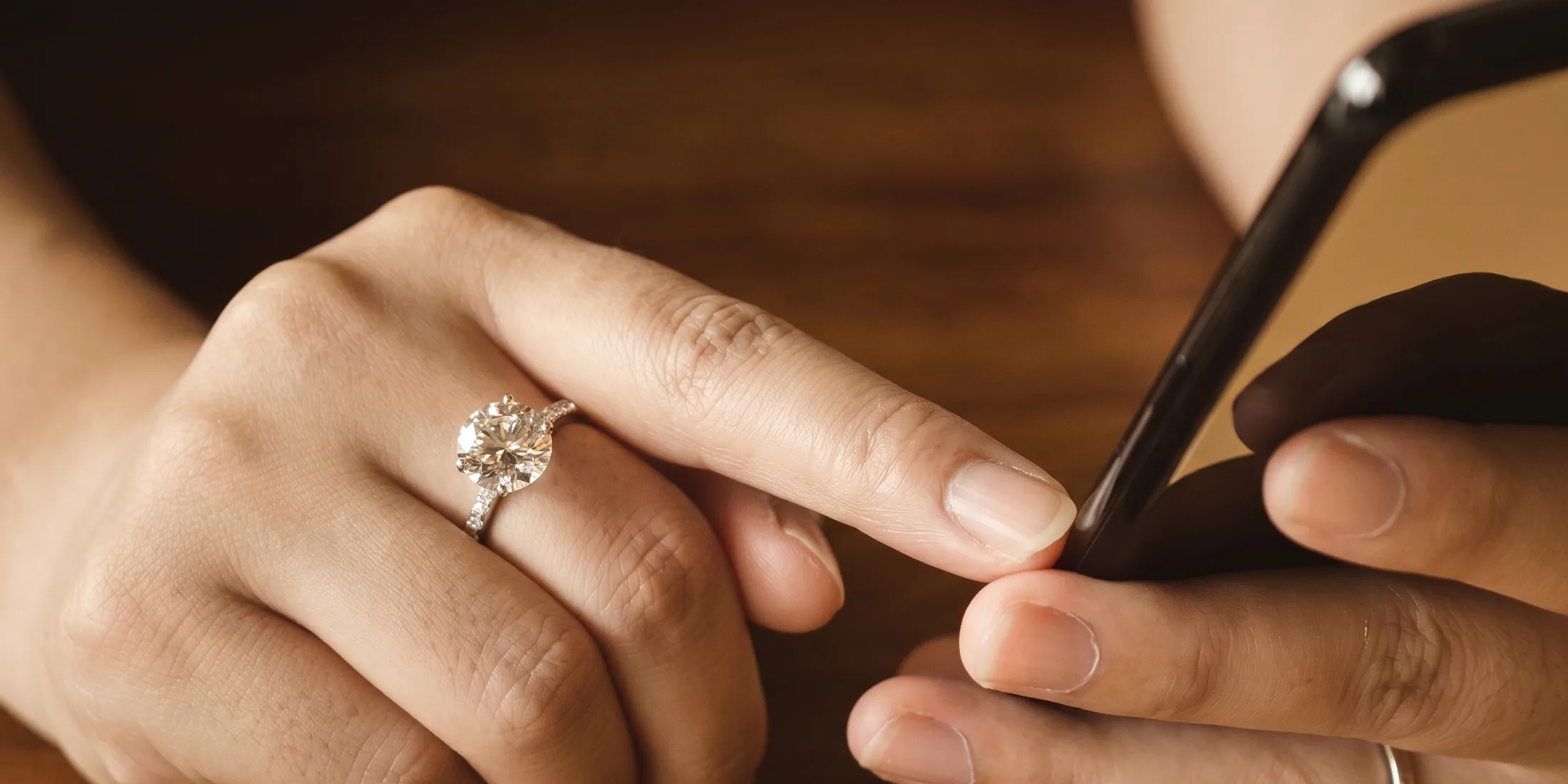 Hands holding a phone, one wearing a diamond ring. Click to browse Erley Diamonds' inventory.