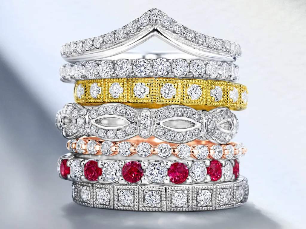 Stack of elegant diamond rings in various styles, including gold and ruby accents. Explore at Falls Jewelers.