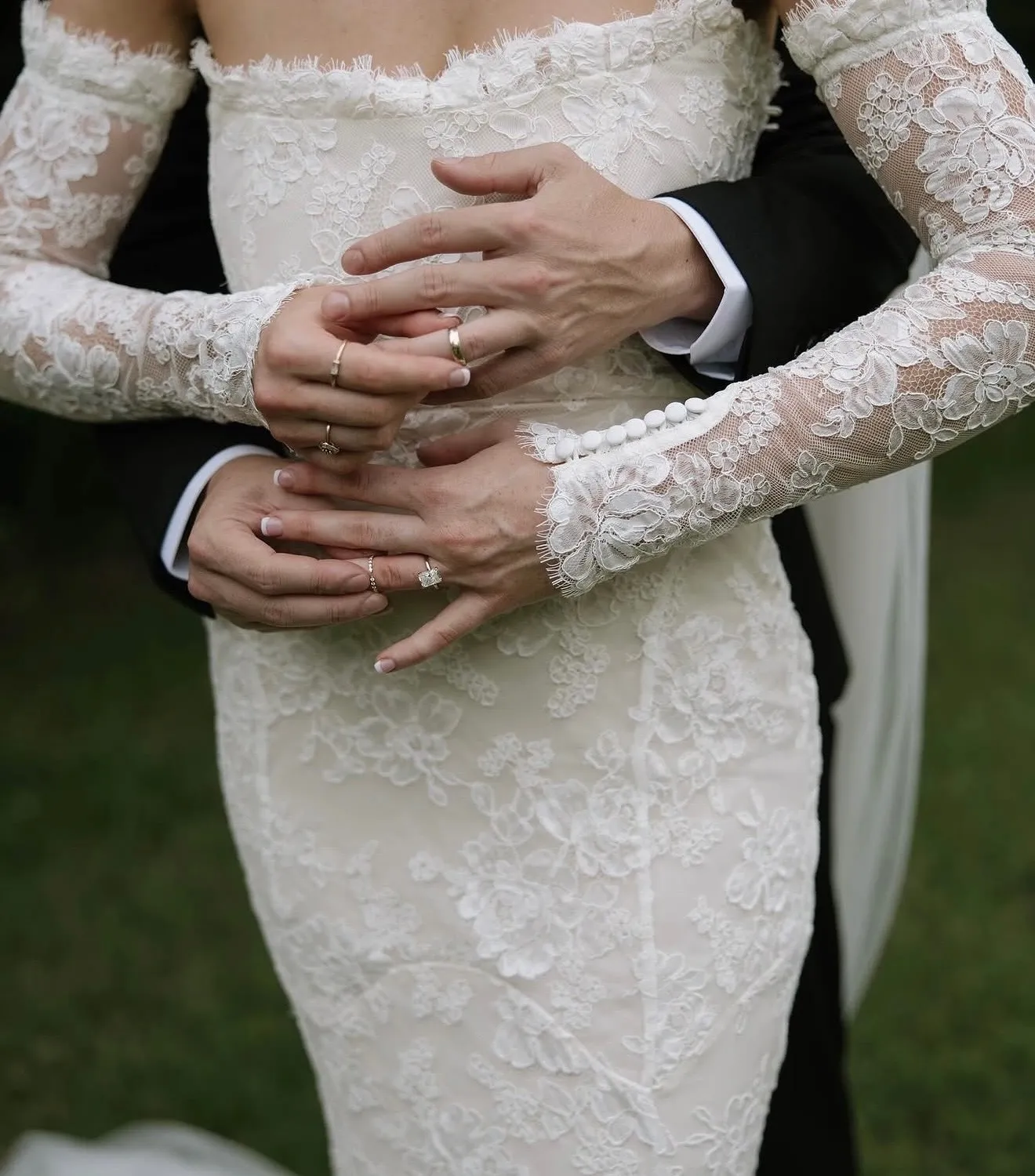 Bride and groom's hands with engagement rings and wedding bands, lace dress detail. Visit Falls Jewelers for bridal jewelry!