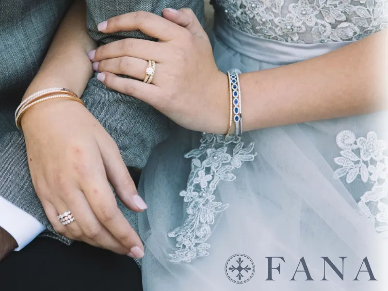 Couple's hands adorned with elegant Fana jewelry, showcasing rings and bracelets. Click to shop Fana Bands at Falls Jewelers.