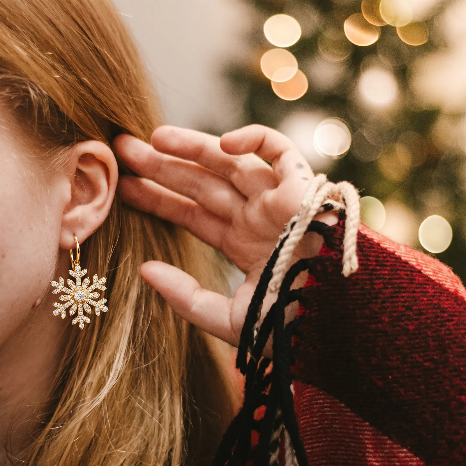 A person wearing a snowflake-shaped earring with a blurred festive background.