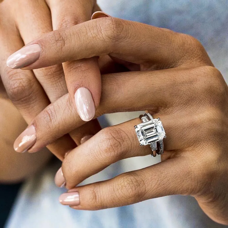 A large emerald-cut diamond ring on the ring finger. Design your own custom engagement ring at Falls Jewelers!