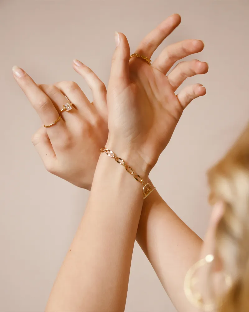Elegant hands adorned with gold rings and a bracelet, showcasing forever jewelry from Falls Jewelers.