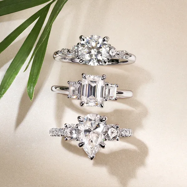 Three elegant engagement rings featuring round, emerald, and pear-shaped diamonds on a soft background. Shop Engagement at Falls
