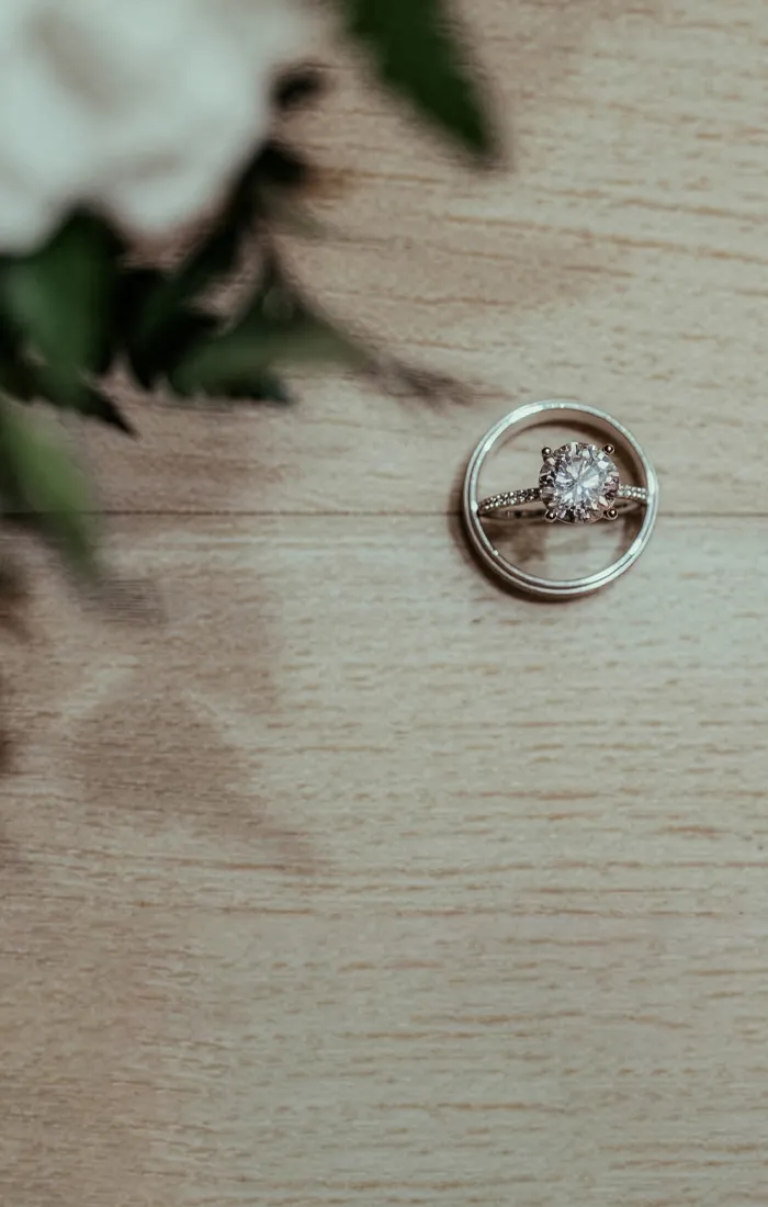 Engagement ring and wedding band displayed on a wooden surface, surrounded by greenery.