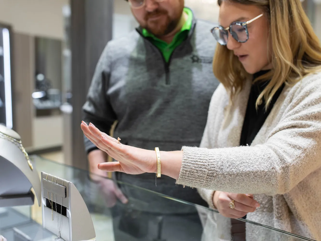 A woman examines jewelry with a man in a store, showcasing a bracelet on her wrist.