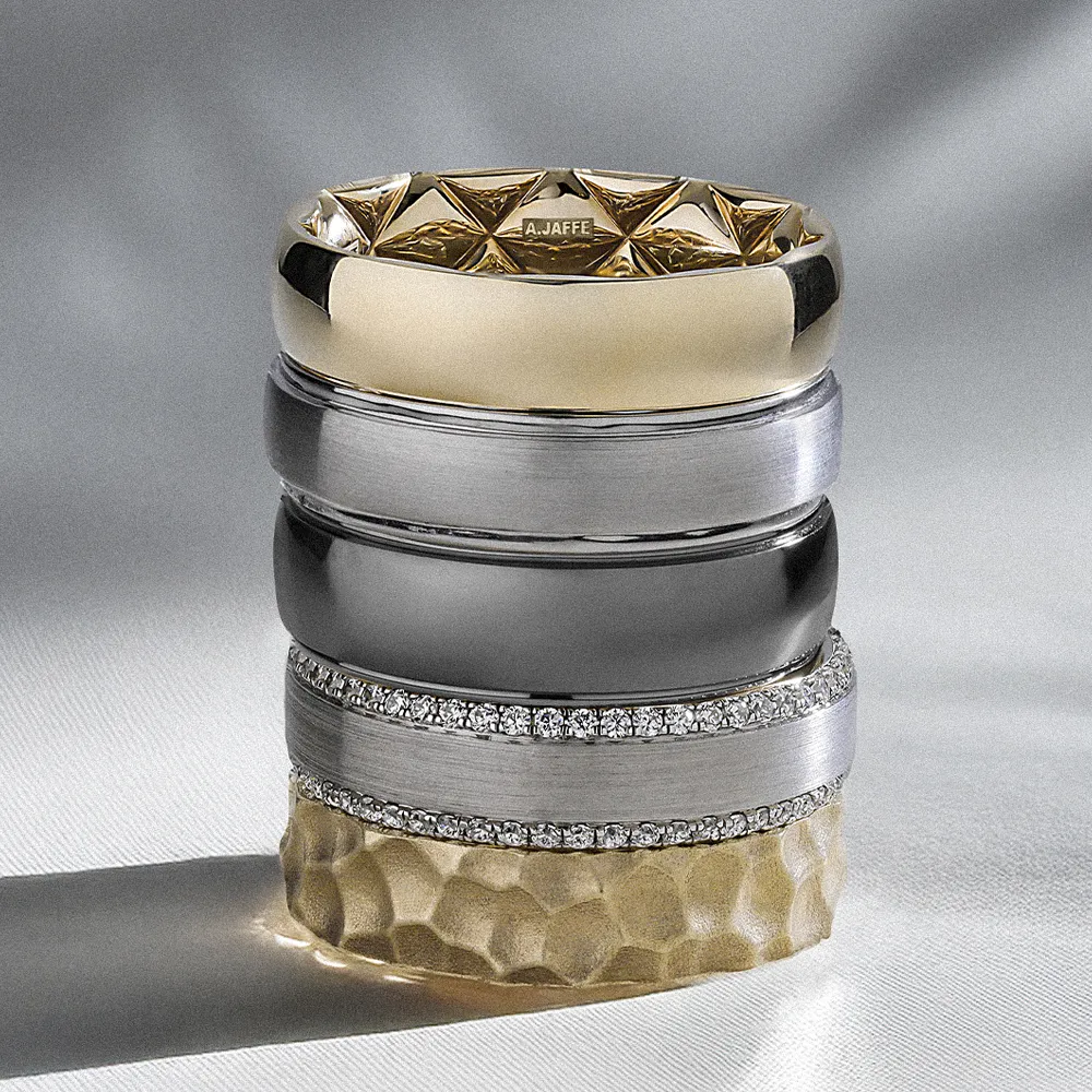 Stack of men's wedding bands in various metals and designs, showcasing elegance and craftsmanship.