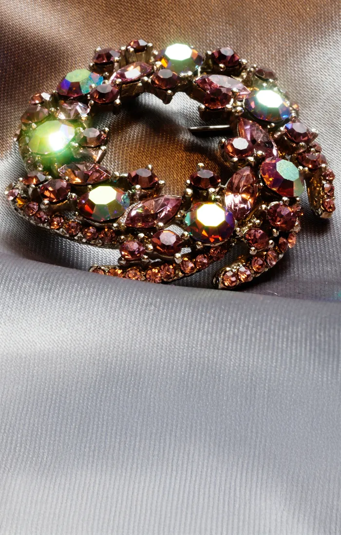 Sparkling brooch with pink and green gemstones on a silky fabric background.