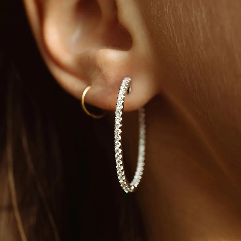 Close-up of a woman's ear featuring a large diamond hoop earring and a small gold hoop.