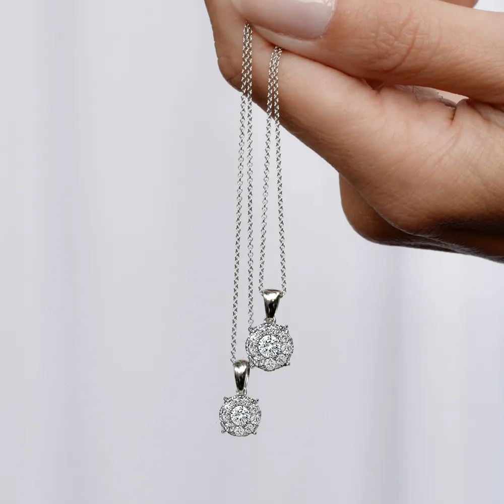 Two sparkling diamond pendants on silver chains held by a hand, showcasing elegant jewelry.
